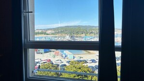 Une vue à travers une fenêtre, avec un ciel dégagé, un parking et un paysage lointain parsemé de bâtiments et de verdure.