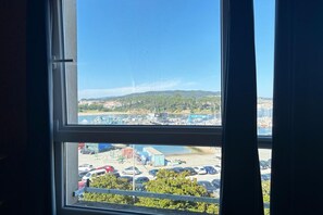 A view through a window with a clear sky, a parking lot, and a distant landscape with buildings and greenery. - Desconectaengalicia El Pescador 2 (Portonovo)