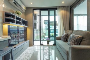 Ein modernes Wohnzimmer mit einer Couch, einem Couchtisch, einem Fernseher und einem Balkon mit Blick auf Gebäude.