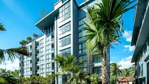 A modern hotel with multiple floors, large windows, and palm trees in the foreground. - Rooftop Pool Condo Walk to Beach, Gym, Wi-Fi c118 (Tambo kamala)