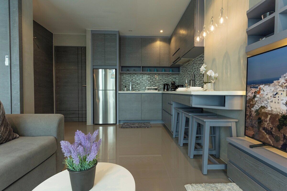 Una cocina moderna con un refrigerador de acero inoxidable, gabinetes grises y una salpicadera de azulejos.