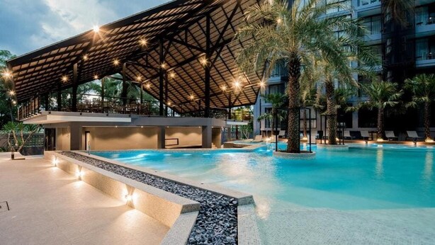 A swimming pool with a covered area, palm trees, and a modern building with balconies. - Rooftop Pool Condo Walk to Beach, Gym, Wi-Fi c118 (Tambo kamala)