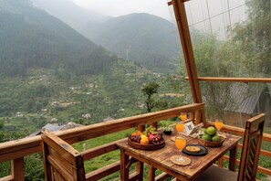 Ein Holztisch mit Obstschale, Keksen und Getränken auf einem Balkon mit Blick auf ein Tal.