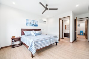 A bedroom with a bed, a nightstand, a ceiling fan, a painting, and a bathroom visible through an open door. - Beautiful, spacious 4-bedroom Penthouse, where luxury meets comfort. (Jaco)