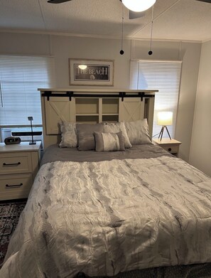 Un dormitorio con cama, mesitas de noche, una lámpara y un cuadro colgado en la pared.