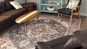 A living room with a sofa, a bench, a chair, a TV, a ceiling fan, and a decorative rug. - Terrific 2-bedroom mobile home,  perfect for bringing your boat (Wilmington)
