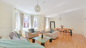 Ein geräumiges Wohnzimmer mit einer Couch, zwei Sesseln, einem Glastisch und einem Essbereich mit einem Holztisch und Stühlen.