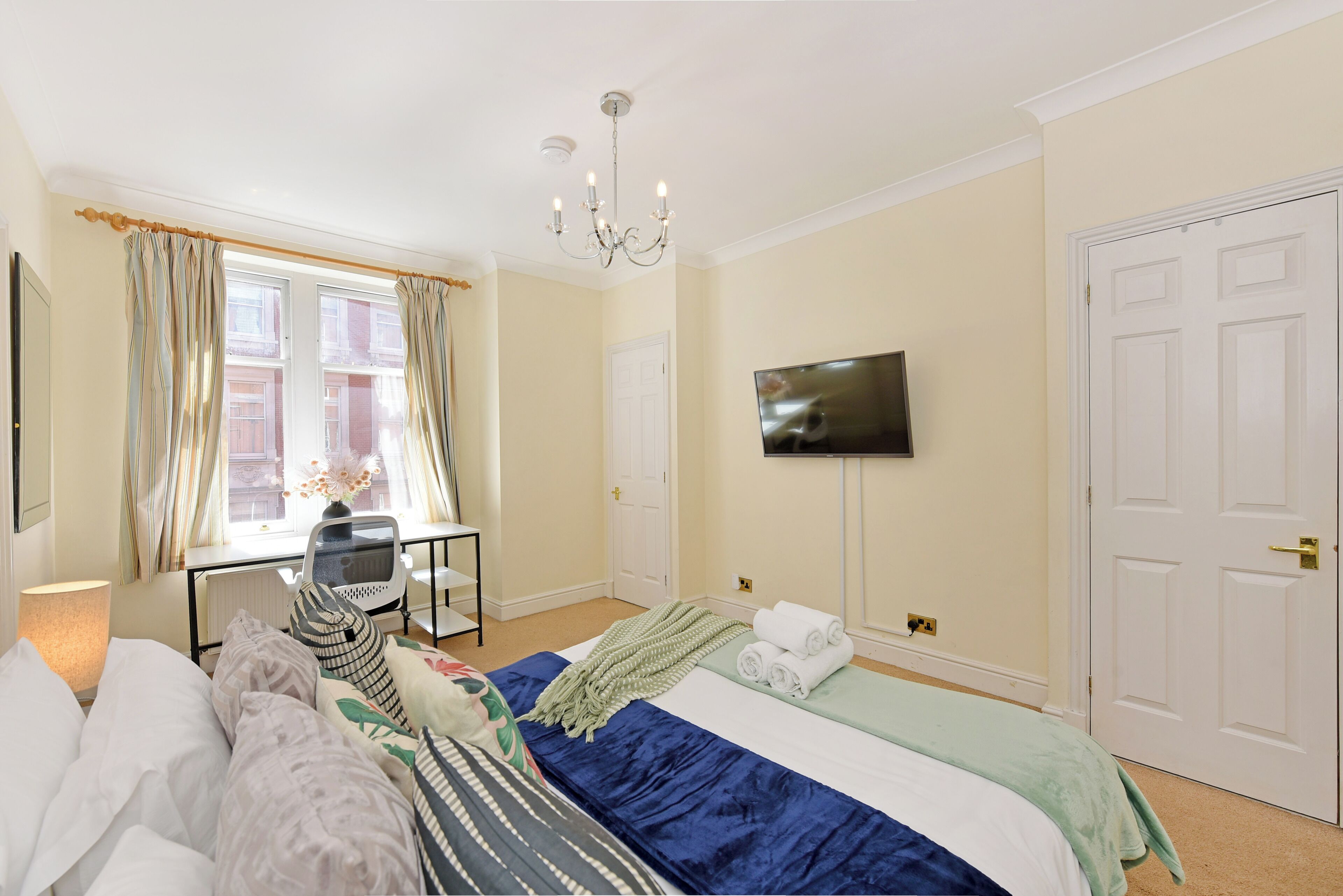 Quarto de hotel com uma cama, televisão, escrivaninha e janela com cortinas.