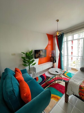 A modern living room with a sofa, TV, and a view of the outside. - Cozy Studio in Nairobi perfect for your city getaway (Nairobi)