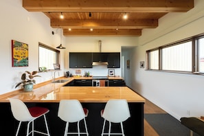 A modern kitchen with a wooden island, bar stools, and large windows.