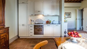 A kitchen with white cabinets, a stove, and a dining table with a fruit bowl. - Apartment in Lucca With Stunning Tuscan Views (Capannori)