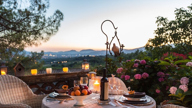 An outdoor dining setup with wicker furniture, a table with a lace tablecloth, candles, a bottle, and a bowl of fruit. - Apartment in Lucca With Stunning Tuscan Views (Capannori)