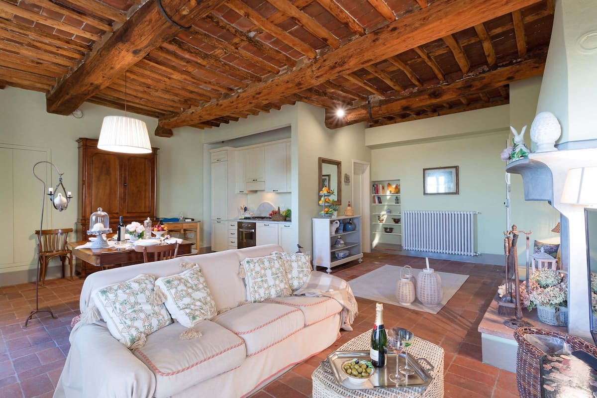 A cozy living room with a wooden ceiling, a sofa, a dining table, and a kitchen area.