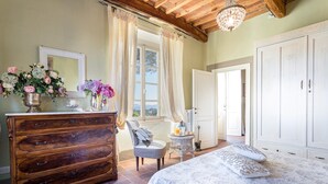 A bedroom with a wooden dresser, a bed with patterned bedding, a chair, a small table with a lamp, and a wardrobe. - Apartment in Lucca With Stunning Tuscan Views (Capannori)