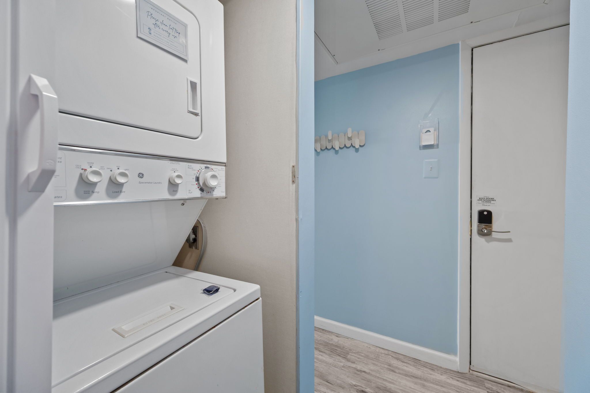 Un área de lavandería con lavadora y secadora de carga frontal, una pared azul y una puerta con cerradura.