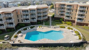 A multi-story hotel with a central pool, outdoor seating, and a view of the water. - Skytide | Oceanfront Balcony + Pool & Beach Access (North Topsail Beach)