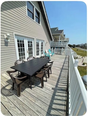 A deck with a table and chairs, a white railing, and a house in the background. - Memory Maker: Cozy 3-bedroom house in quaint Oak Island steps to the beach (Oak Island)