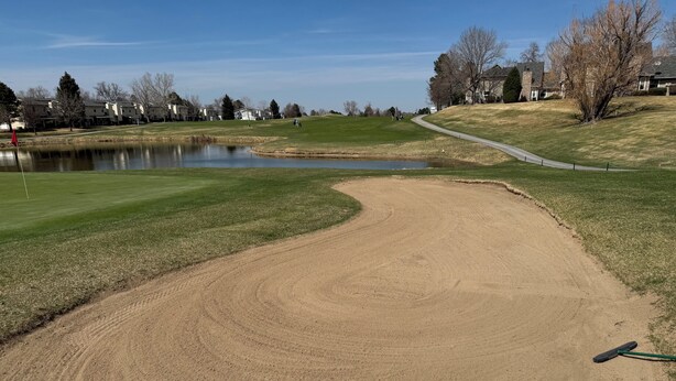 Ein Golfplatz mit einem Sandbunker, einem Teich und einem Weg.