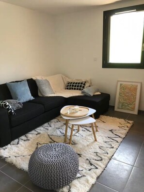 A living room with a black sofa, a round coffee table, a grey pouf, and a white shag rug. - ⛰️ Spacious, comfortable apartment at the foot of the Ancelle slopes - Alps (Ancelle)