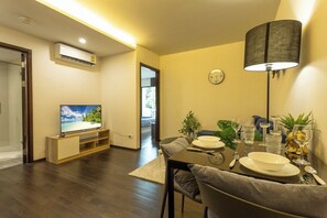 A modern living room with a flat-screen TV, dining table set for two, and a lamp. - Beach Walk Condo Poolside Retreat by the Sea C123 (Tambon Rawai)