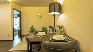 A dining area with a table set for two, a clock on the wall, and a lamp. - Beach Walk Condo Poolside Retreat by the Sea C123 (Tambon Rawai)