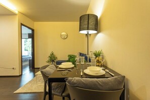 A dining area with a table set for two, a clock on the wall, and a lamp. - Beach Walk Condo Poolside Retreat by the Sea C123 (Tambon Rawai)