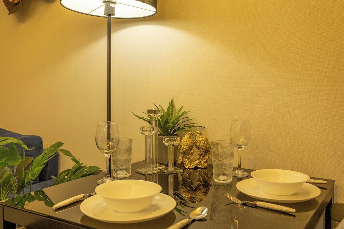 A dining table set with white bowls, glasses, and cutlery, a decorative pineapple centerpiece, and a tall floor lamp.