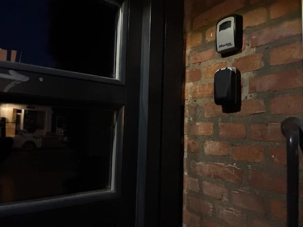 Un mur de briques sur lequel sont fixés deux appareils, un cadre de porte et le reflet d’un bâtiment à l’extérieur.