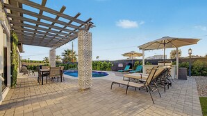 En täckt uteplats med pool, utomhusmöbler och en pergola.
