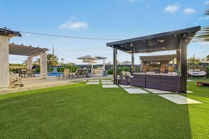 Una zona de terrassa exterior ben cuidada amb una zona de barbacoa, espais per seure i una piscina.