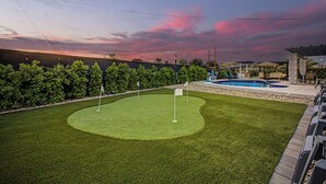 En välskött gräsmatta med en puttinggreen, en swimmingpool och ett möblerat område under tak.