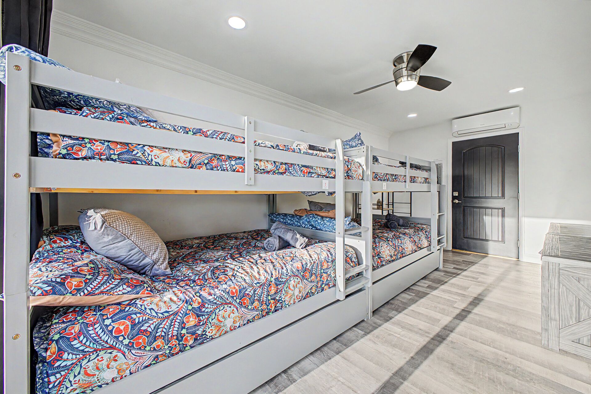 A bunk bed room with a ceiling fan, a door, and a patterned bedspread.