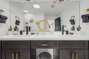 Ein modernes Badezimmer mit zwei Waschbecken, einem großen Spiegel und dekorativen Wandleuchten.