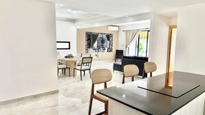 Una sala de estar moderna con comedor, un sofá negro y un televisor.