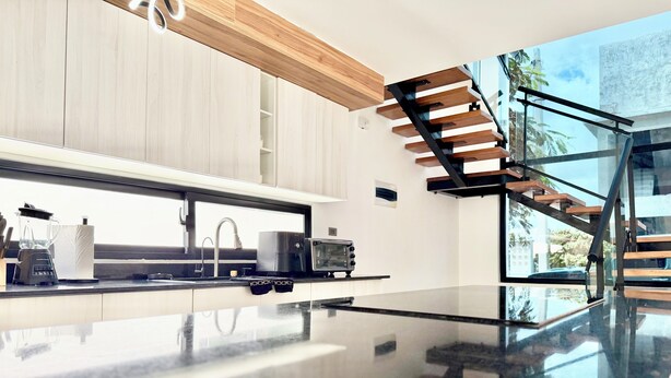 Una cocina moderna con una isla grande, horno empotrado y escalera de cristal.