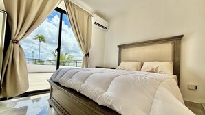 Un dormitorio con una cama grande, cabecera de madera y vista a palmeras a través de una ventana.