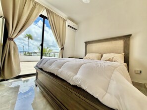 A bedroom with a large bed, a wooden headboard, and a view of palm trees through a window.