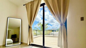 Una habitación con un gran ventanal corredero que da a un balcón con vistas a palmeras y un edificio.