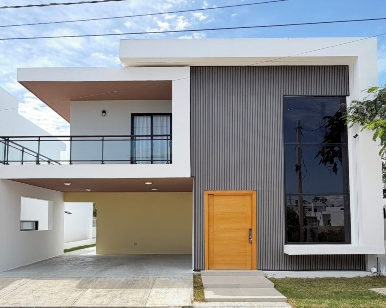 Une maison moderne à deux étages, dotée d’un balcon, d’une grande fenêtre et d’une porte en bois.