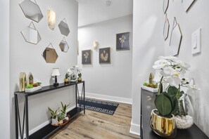 A hallway with a console table, wall-mounted mirrors, framed artwork, and potted plants. - Luxury  4-bedroom house in Atlanta (Atlanta)