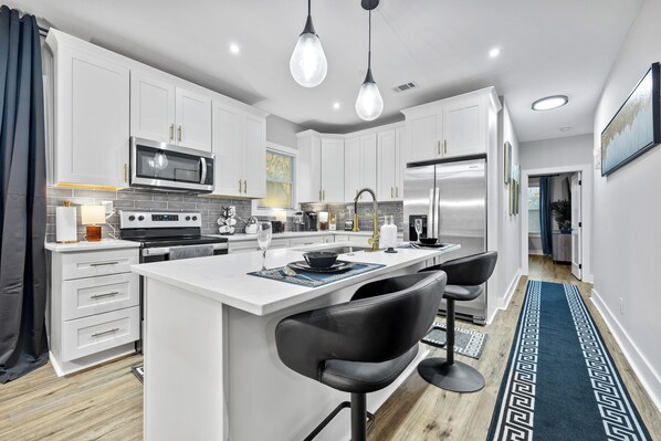 A modern kitchen with white cabinetry, stainless steel appliances, a central island with bar stools, and pendant lighting. - Luxury  4-bedroom house in Atlanta (Atlanta)