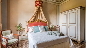 A bedroom with a four-poster bed, a wooden chair, a white wardrobe, and a patterned floor. - Luxury Villa With Pool in Lucca (Capannori)