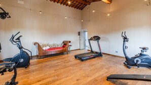 A spacious room with a wooden floor, a treadmill, an elliptical, and a sofa. - Luxury Villa With Pool in Lucca (Capannori)