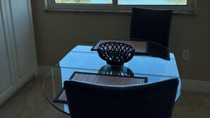 Un coin repas avec une table et des chaises en verre, un vase décoratif, et une vue sur une étendue d’eau et des bâtiments.