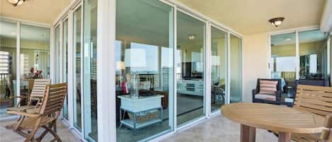 A spacious patio with a sliding glass door leading to a kitchen area, wooden furniture, and a view of the cityscape.