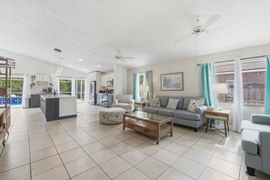 A spacious living area with a sofa, ottoman, coffee table, and a kitchen in the background. - Spacious 4BR Pool Home Peaceful Views (Kissimmee)