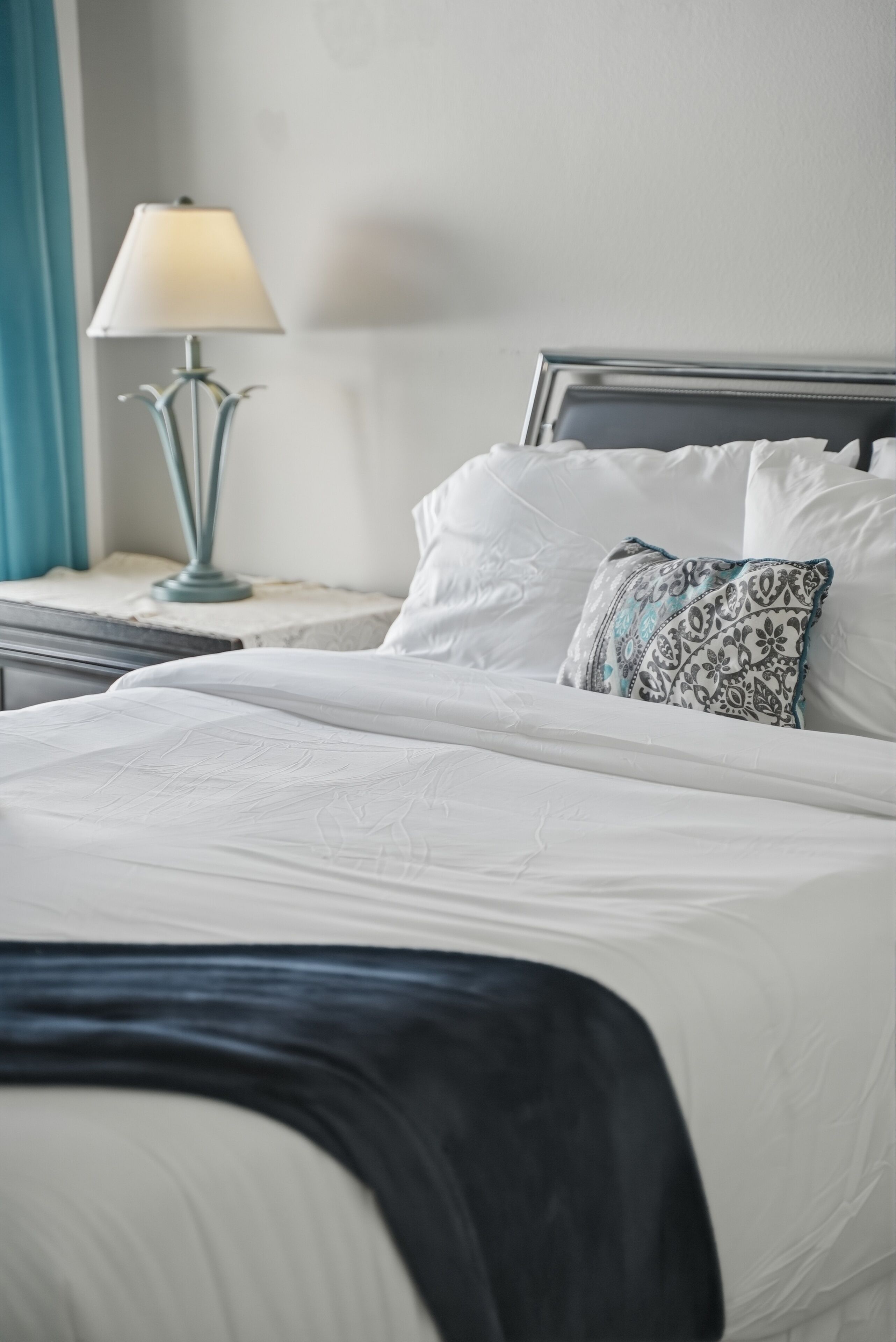 A neatly made bed with white linens, a patterned pillow, and a bedside lamp on a nightstand.
