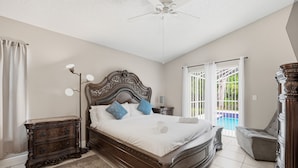 Un dormitorio con una cama grande, una mesita de noche, una silla y vistas a una piscina.