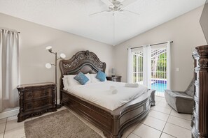 A bedroom with a large bed, a nightstand, a chair, and a view of a swimming pool. - Spacious 4BR Pool Home Peaceful Views (Kissimmee)