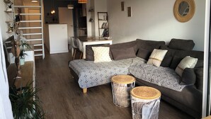 A modern living room with a sectional sofa, two round side tables, a dining area with a table and chairs, and a staircase leading to an upper level. - 🌞🪸 Le Corail 🪸 - Apartment 3 bedrooms 6 people - 🦩 Le Grau Du Roi 🦩🌞 (Le Grau-du-Roi)